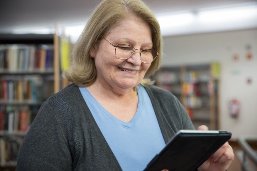 Mujer mayor con tablet en biblioteca pública
